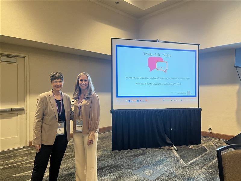 Two professional women standing side by side next to a presentation 
