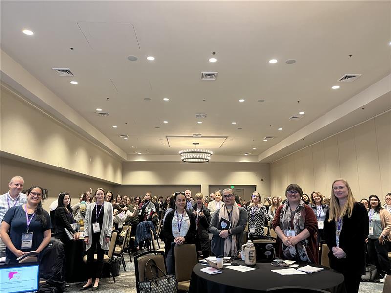 A large room of workshop participants standing 