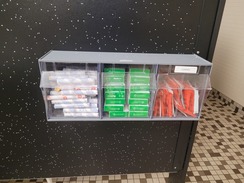 A shelf with menstrual products affixed to a bathroom stall