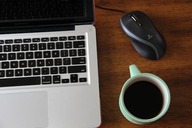 A laptop on a desk next to a cup of coffee and mouse.