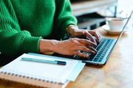 A person sitting at a table with a laptop, notebook, and pencil
