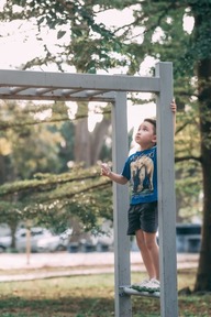 Child standing on playground structure, looking upward while holding the frame.