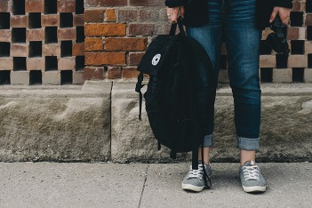 student holding a backpack in front of a brick wall
