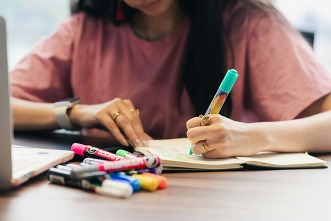 A person writing in a notebook, using colorful pens and highlighters