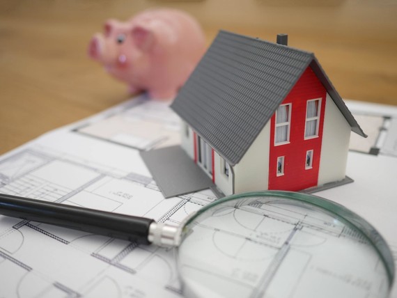 Tierra Mallorca on Unsplash: Red & white model house, magnifying glass, and piggy bank sitting on plans. 