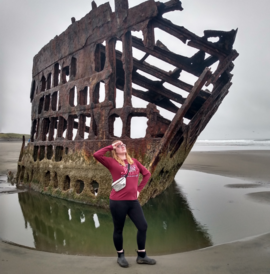 woman with pink hoodie, posing in front of ship wreck