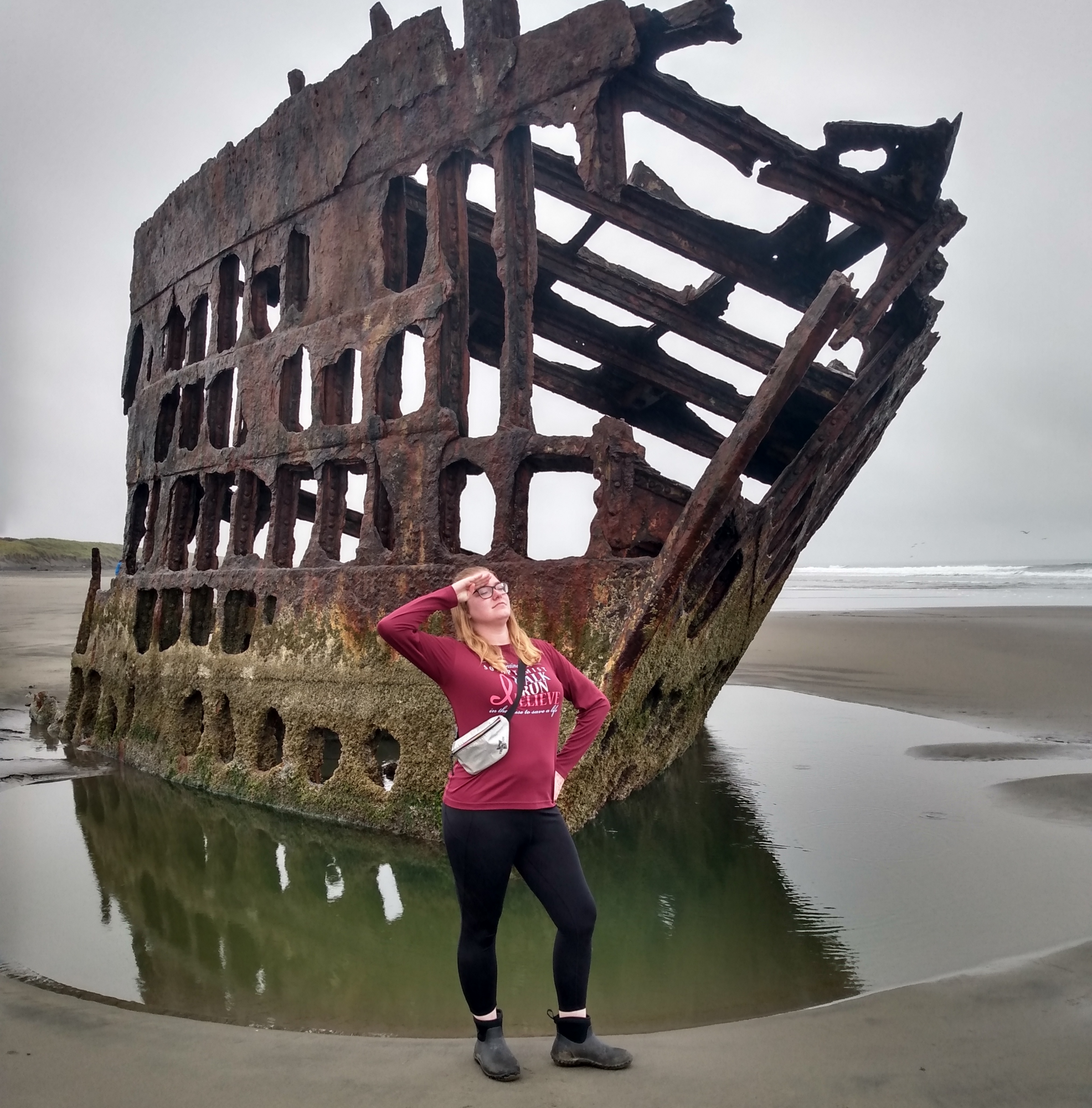 woman in pink hoodie, posing in front of ship wreck