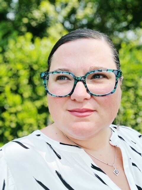 white woman wearing glasses in front of shrubbery