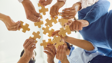 white background with many hands holding wooden puzzle pieces