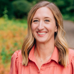 woman smiling wearing a coral dress and a heart necklace