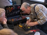 A man with tools testing electonic equipment while two people look on