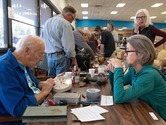 A man at a table tests a clock while two people look on