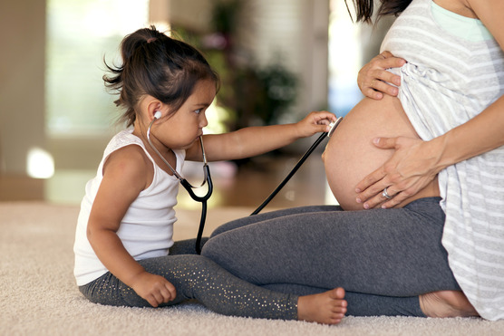 little girl holding a stethescope to a pregnant woman's belly