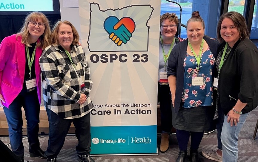 OHA's Suicide Prevention Team members surround a banner that reads, "OSPC 23: Hope Across the Lifespan: Care in Action"