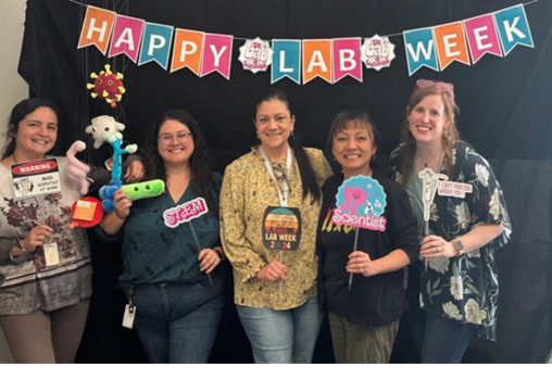 five women standing beneath a banner that says "Happy Lab Week"