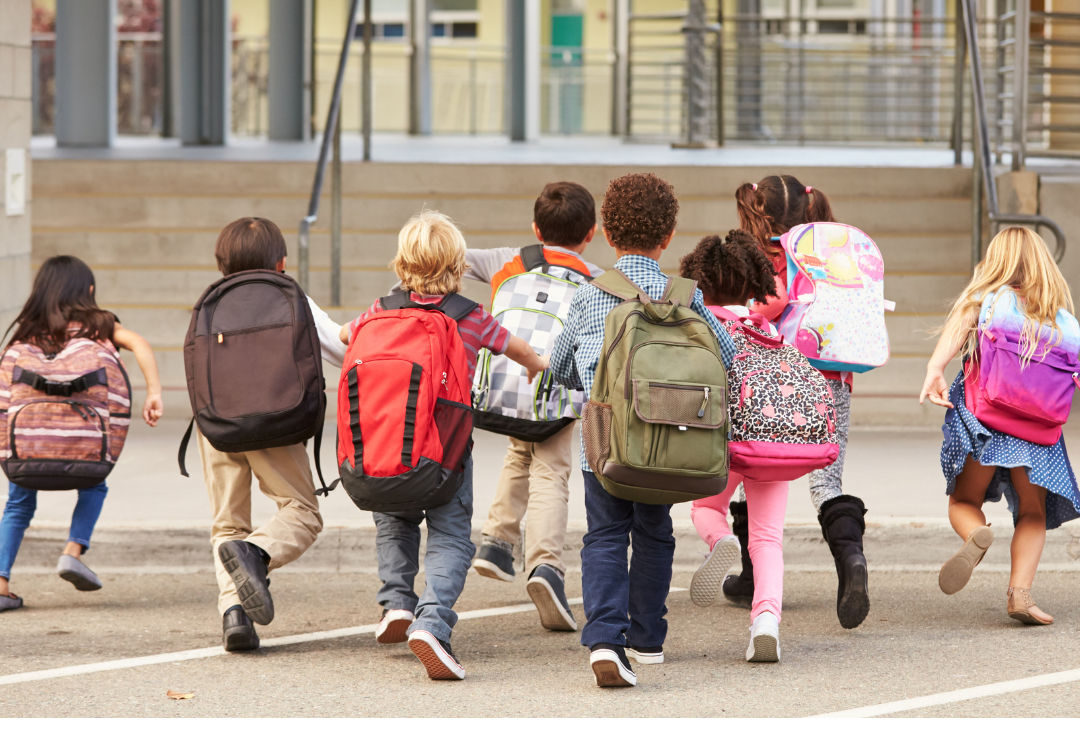 photo of kids wearing backpacks running into a school