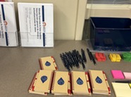 A table from the Open House events. It is covered in presentation materials, notebooks, and sticky note pads. 