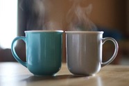 Two steaming blue and brown mugs sitting side by side on a counter.