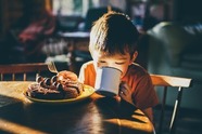 A child drinking out of a mug at a table, sitting behind a plate of waffles