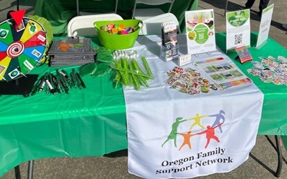 Oregon Family Support Network's resource table featuring stickers, pencils, cards, tote bags and other handouts about the network