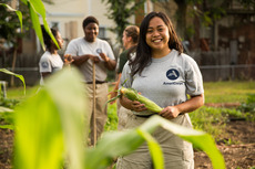 Smiling AmeriCorps member harvesting corn.