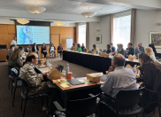 Tech Consortium members seated around a u-shaped conference table listen to panelists. 