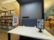 Interior of SOWIB kiosk shows workspace, tablet showing Engage by Cell home screen, and flier with more info. Library shelves in background.