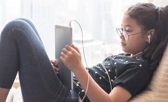 Young girl layback on a chair with a computer tablet in her hands and with earbuds in her ears.