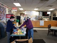 Two men in masks organizing packaged food on a long table 