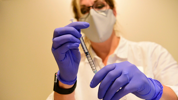 Nurse with mask, glasses and purple gloves holding syringe 