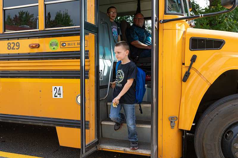young boy with backpack exiting a stopped school bus 