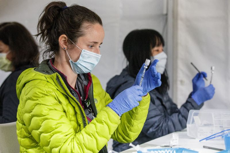 two women in reusable masks in jackets administering vaccine shots