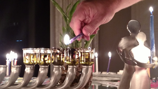 A silver menorah with a hand lighting one of the candles