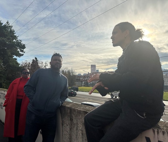 Rep Nelson leaning on a wall talking to AVT staff in front of the Willamette River