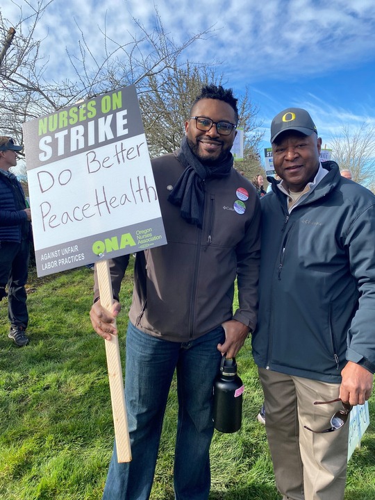 Representative Nelson stands with Senator Manning holding a "Do Better PeaceHealth" sign.