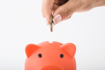 Stock photo of a pink piggy bank with a coin being inserted