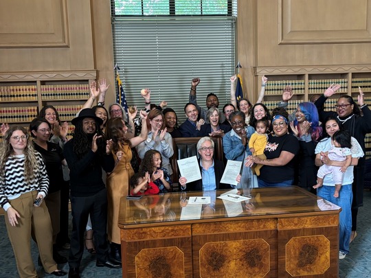 A group of advocates for Momnibus behind gov kotek as she signs the bill