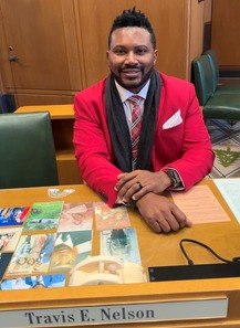 Rep Nelson wearing a red suit while sitting at his desk on the House Floor
