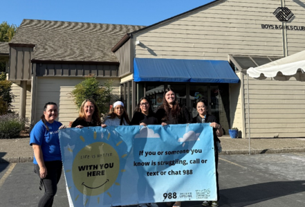 Image of Mental Health Promotion and Boys and Girls Club Staff holding 988 banner Infront of the Boys and Girls Club