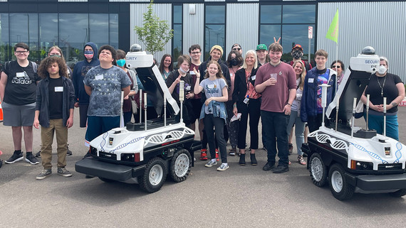 Technology interns and coding students from Cascade and Pacific Academies pose with Eve and Ray, two of Genentech's security robots