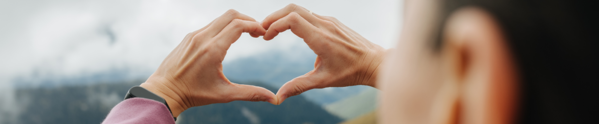 person making a heart shape with their hands with mountains in background