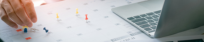a hand pushes thumbtacks on a paper calendar