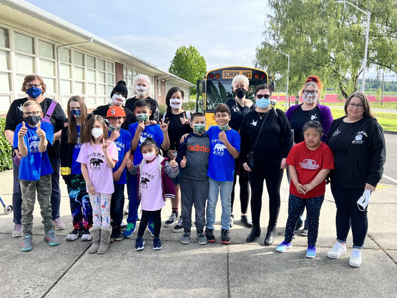 Students and their teachers pose outside their school in front of a school bus