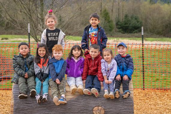 preschoolers sit on a log on the playground