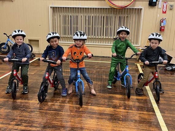 five preschoolers ride balance bikes in a gym