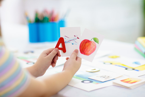 a child holds a red letter A next to an illustration of an airplane and an apple