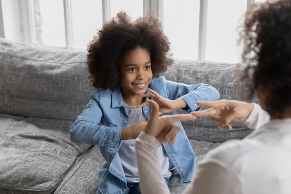 A young girl signs with her mom while she sits on the couch