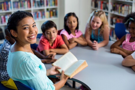 A teacher looks at the camera for a moment while reading to children