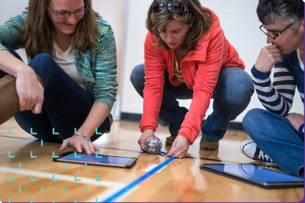 three teachers hold ipads and a small robot on a gym floor