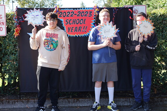 three boys hold up signs against at black backdrop and a sign that says 2022-23 school year
